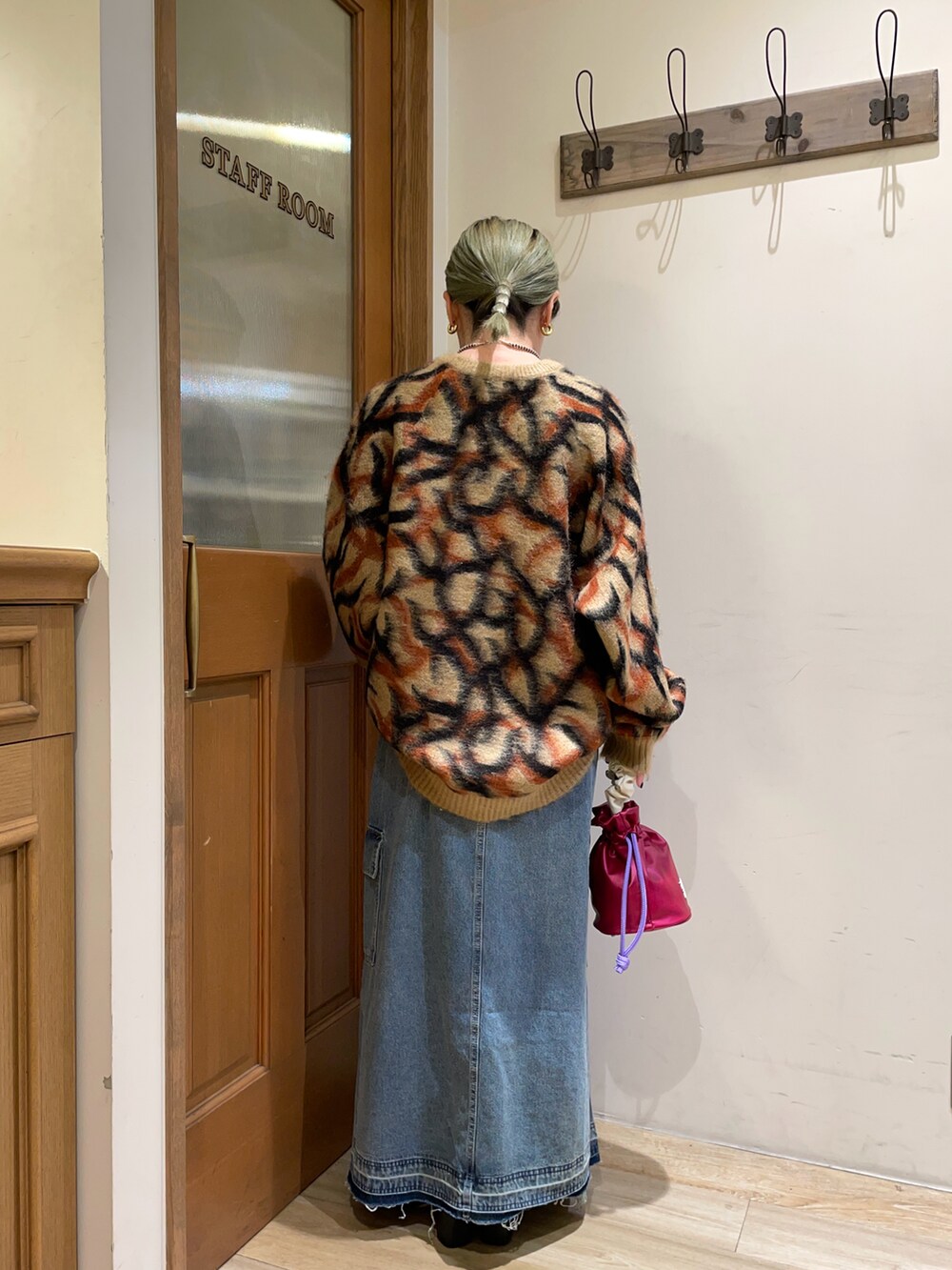 ブラウン系のニット/セーター、ブラック系のハンドバッグ、ブルー系のスカートを着用したレディースの秋コーディネートの2枚目の写真