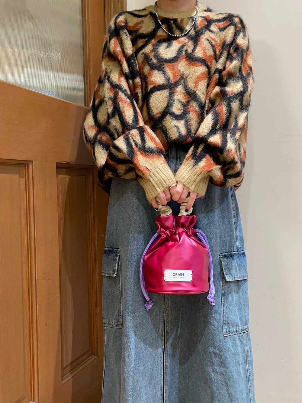 ブラウン系のニット/セーター、ブラック系のハンドバッグ、ブルー系のスカートを着用したレディースの秋コーディネートの5枚目の写真