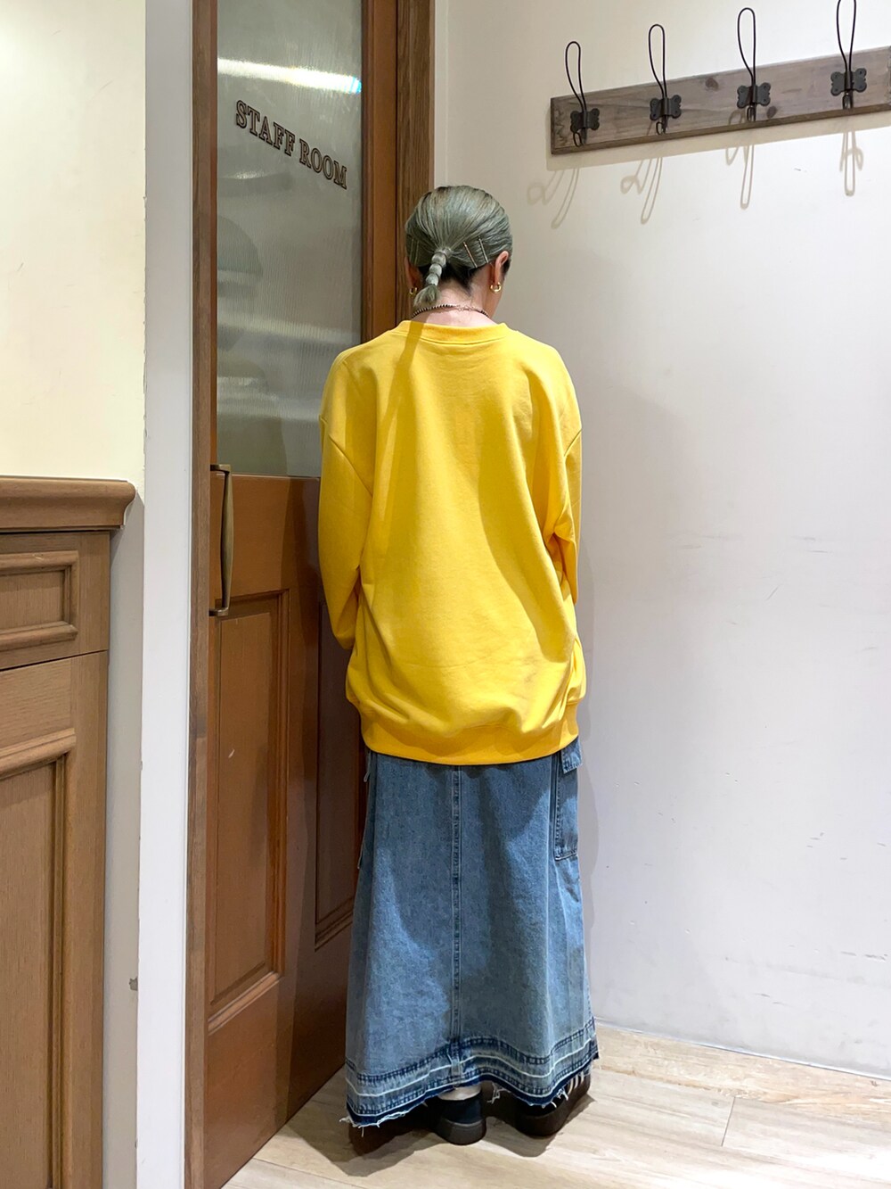 イエロー系のスウェット、ブルー系のスカート、ブラック系のハンドバッグを着用したレディースの秋コーディネートの2枚目の写真