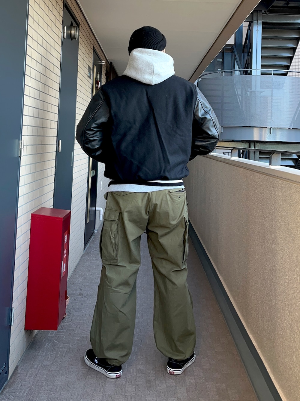 グレー系のパーカー、ブラック系のスタジャン、グリーン系のカーゴパンツを着用したメンズの冬コーディネートの2枚目の写真