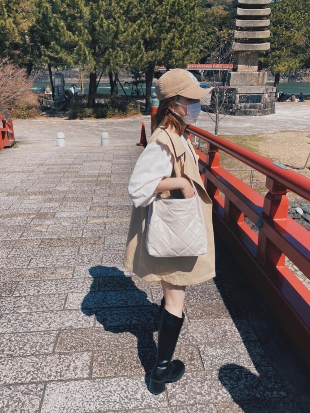 ホワイト系のショルダーバッグ、ベージュ系のトレンチコート、ブラック系のブーツを着用したレディースの秋コーディネートの2枚目の写真