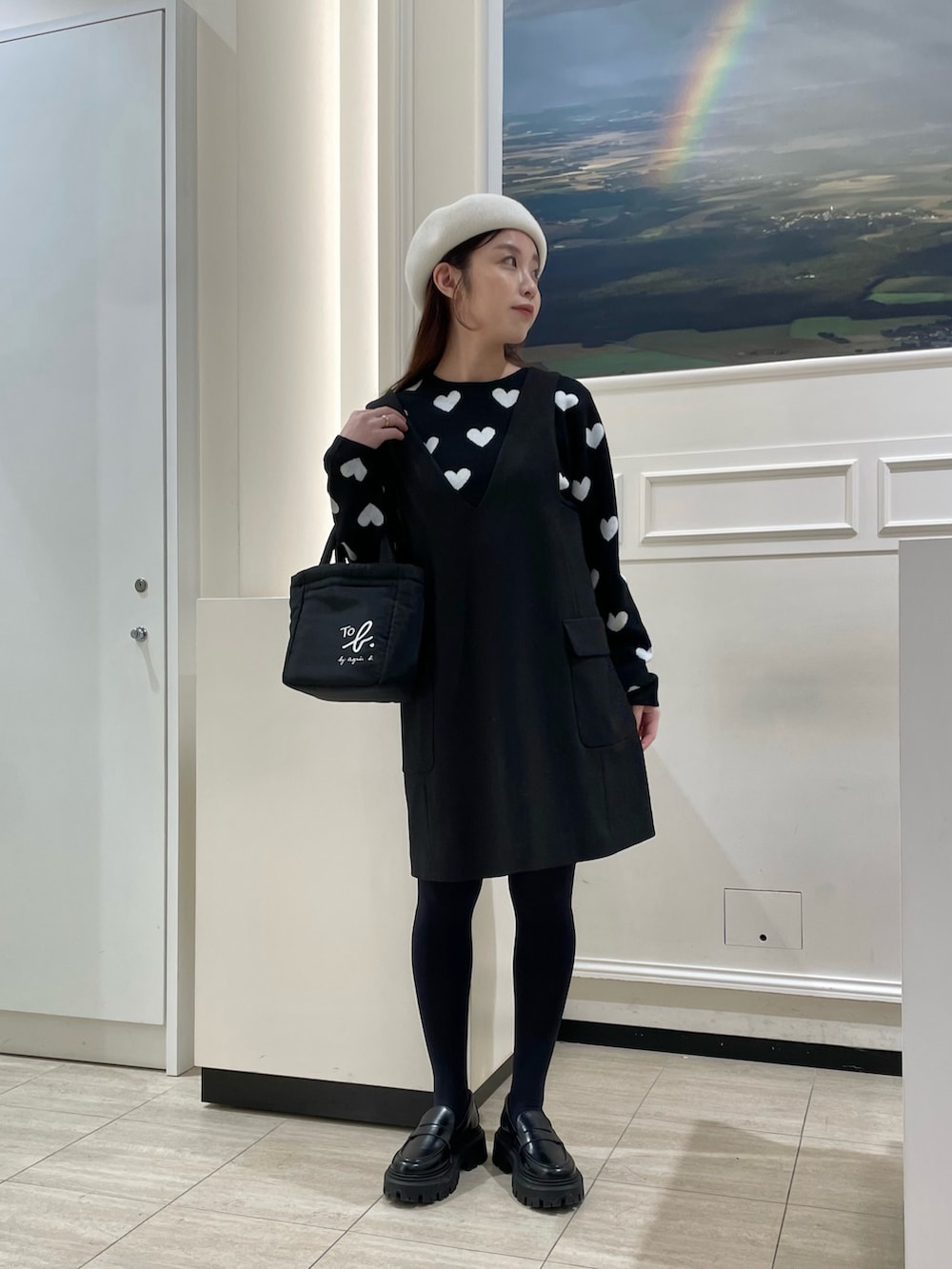 ブラック系のニット/セーター、ブラック系のジャンパースカート、ブラック系のエコバッグ/サブバッグを着用したレディースの冬コーディネートの2枚目の写真