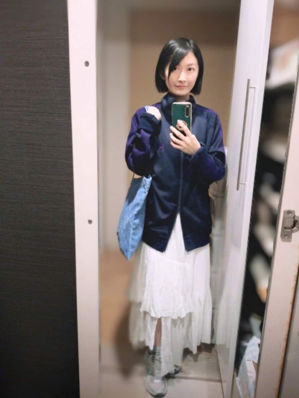 ブルー系のトートバッグ、ホワイト系のスカート、ブラック系のジャケット/アウターを着用したレディースの冬コーディネートの2枚目の写真