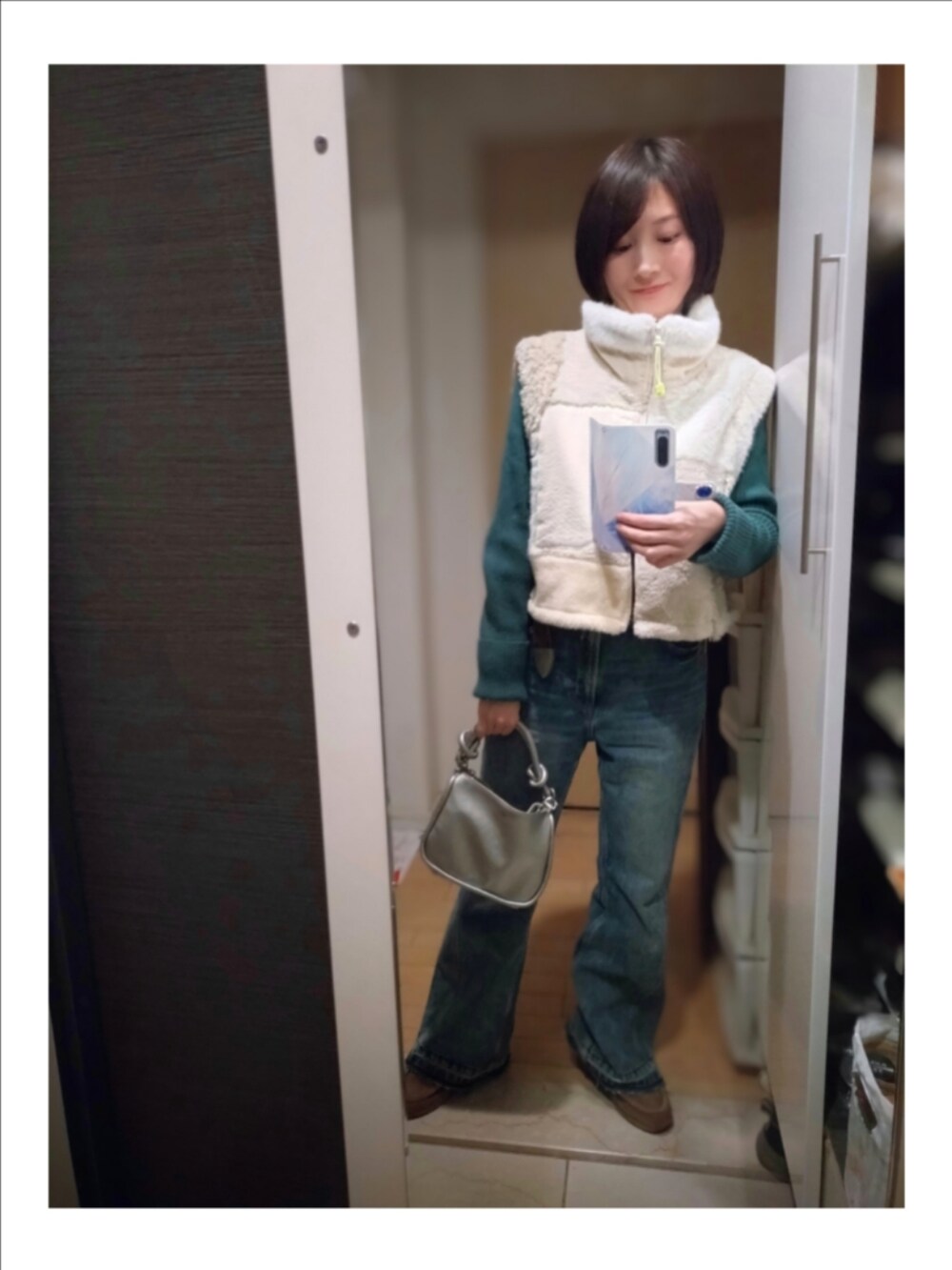 ホワイト系のベスト、シルバー系のショルダーバッグ、ブルー系のデニムパンツを着用したレディースの冬コーディネートの2枚目の写真