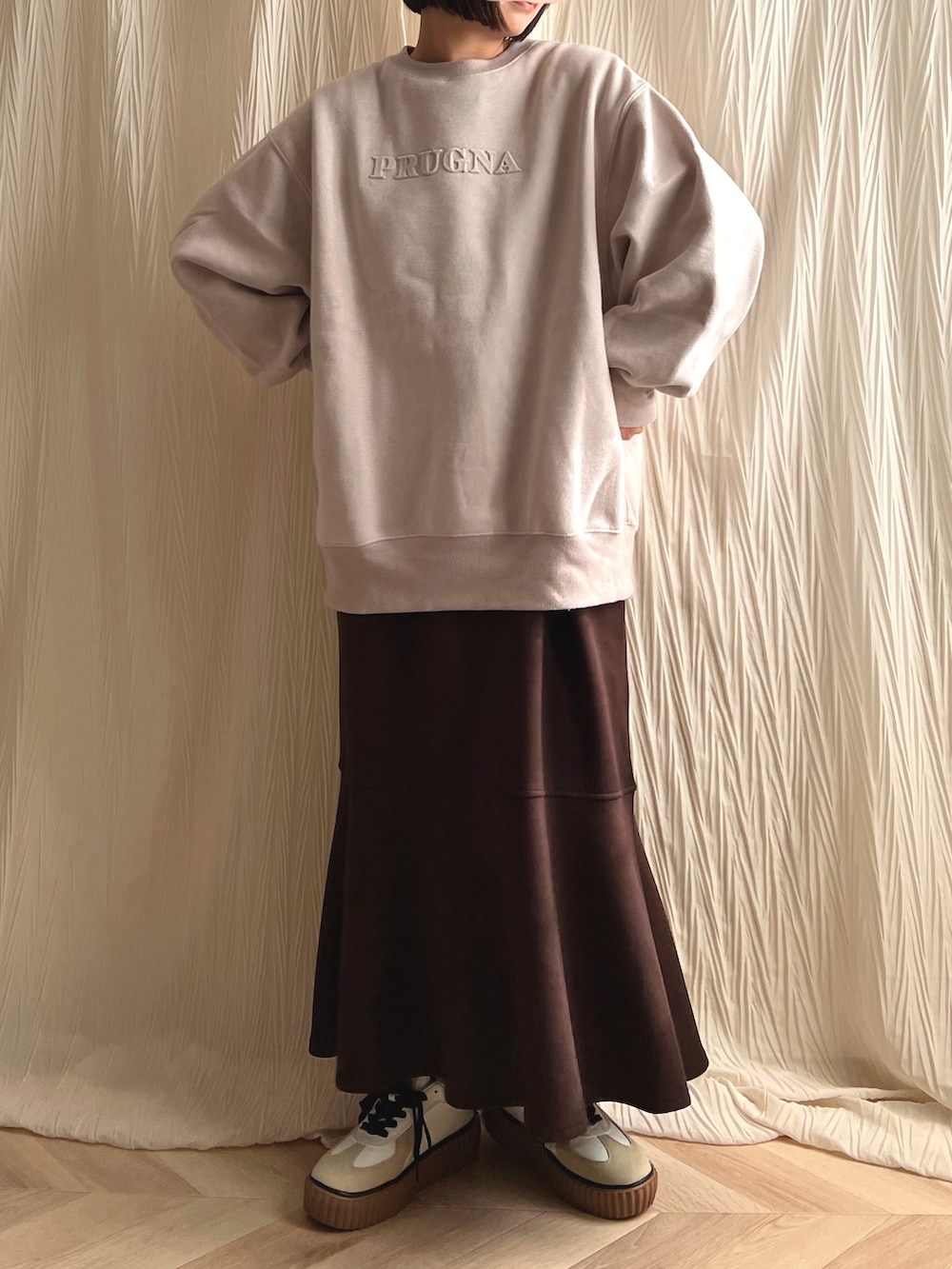 ピンク系のスウェット、ブラウン系のジャンパースカート、ブラウン系のスニーカーを着用したレディースの春コーディネートの2枚目の写真