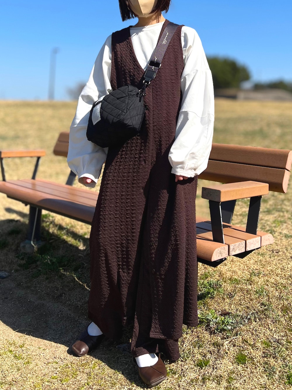 ホワイト系のTシャツ/カットソー、ブラック系のショルダーバッグ、ブラウン系のジャンパースカートを着用したレディースの春コーディネートの2枚目の写真