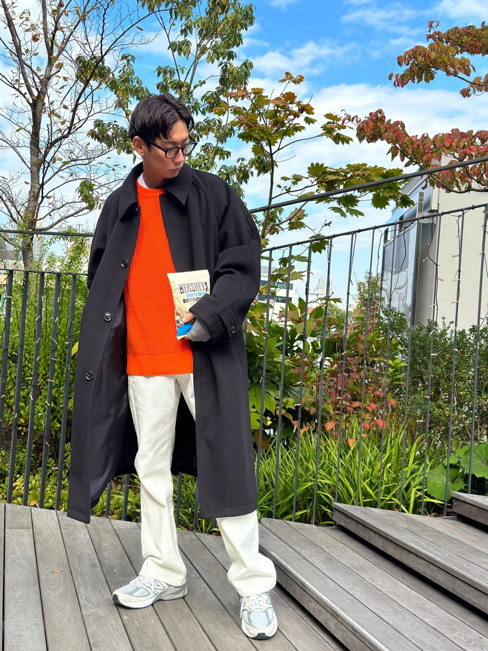 ブラック系のステンカラーコート、オレンジ系のニット/セーター、ホワイト系のTシャツ/カットソーを着用したメンズの秋コーディネートの2枚目の写真