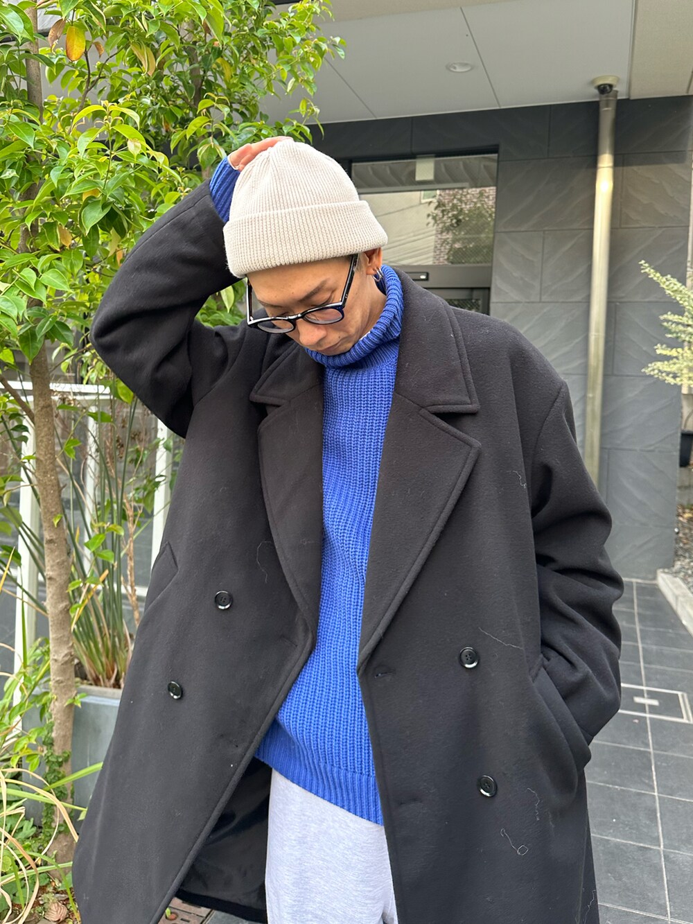 ブラック系のチェスターコート、ブルー系のニット/セーター、グレー系のスウェットパンツを着用したメンズの冬コーディネートの4枚目の写真