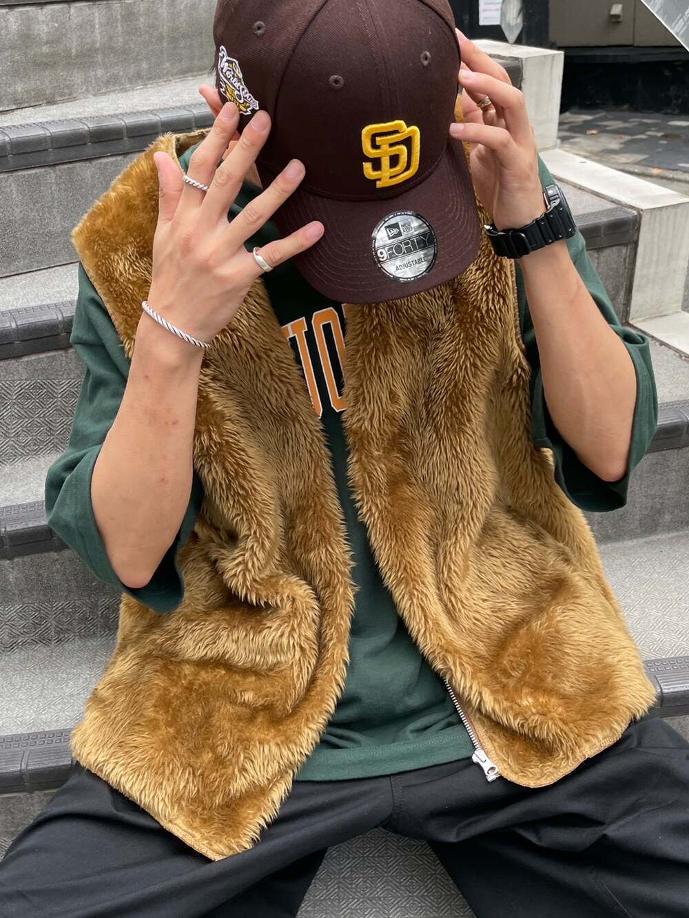 ブラウン系のベスト、グリーン系のTシャツ/カットソー、ブラック系のカーゴパンツを着用したメンズの夏コーディネートの2枚目の写真