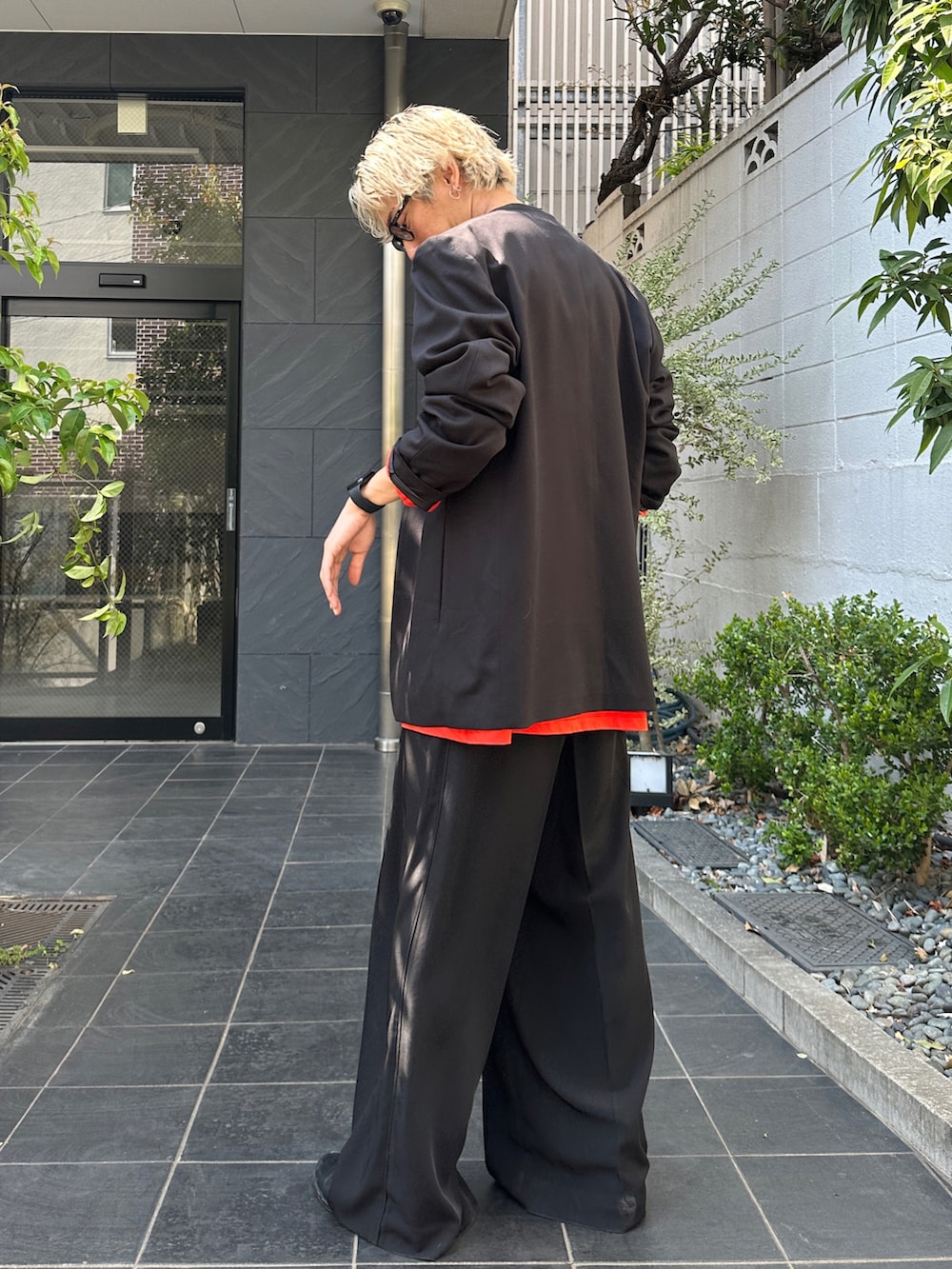 ブラック系のテーラードジャケット、オレンジ系のTシャツ/カットソー、ブラック系のスラックスを着用したメンズの春コーディネートの3枚目の写真