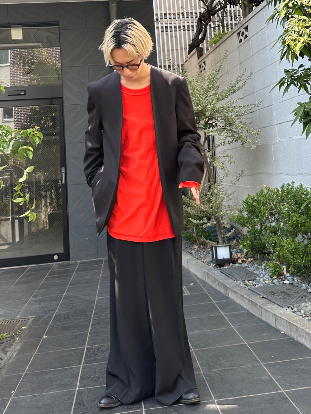 ブラック系のテーラードジャケット、オレンジ系のTシャツ/カットソー、ブラック系のスラックスを着用したメンズの春コーディネートの2枚目の写真