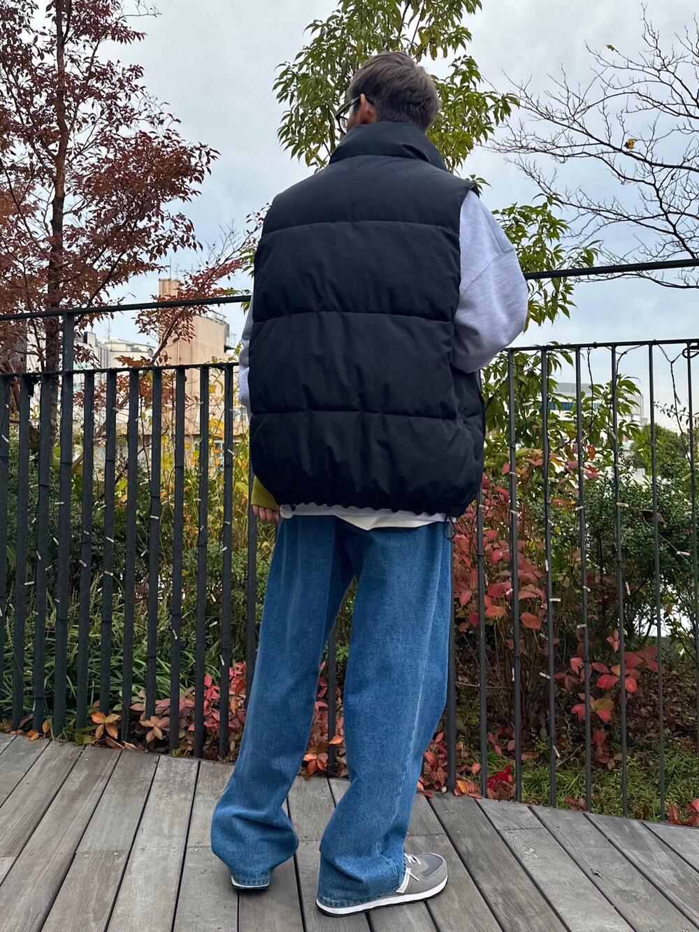 ブラック系のダウンベスト、ベージュ系のスウェット、ブルー系のデニムパンツを着用したメンズの秋コーディネートの2枚目の写真