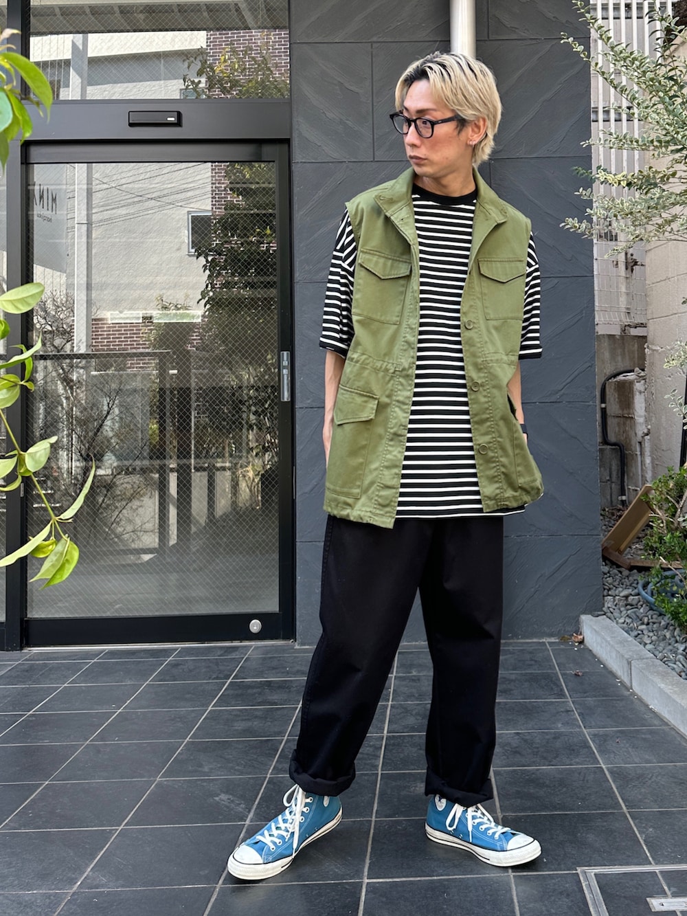 グリーン系のベスト、ブラック系のTシャツ/カットソー、ブラック系のチノパンツを着用したメンズの春コーディネートの3枚目の写真
