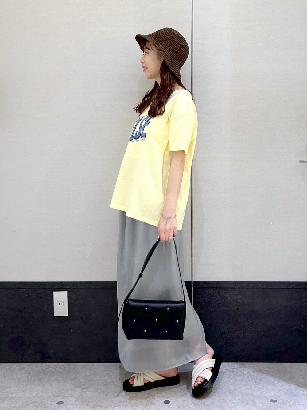 イエロー系のTシャツ/カットソー、グレー系のスカート、ブラック系のショルダーバッグを着用したレディースの春コーディネートの2枚目の写真