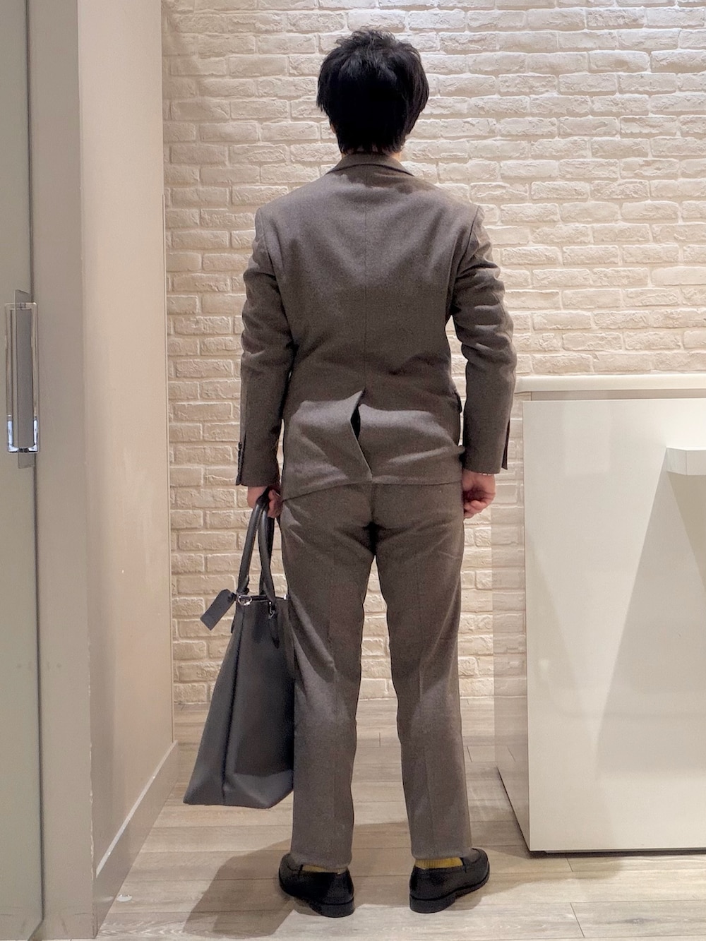グレー系のテーラードジャケット、ブラック系のニット/セーター、グレー系のスラックスを着用したメンズの冬コーディネートの5枚目の写真