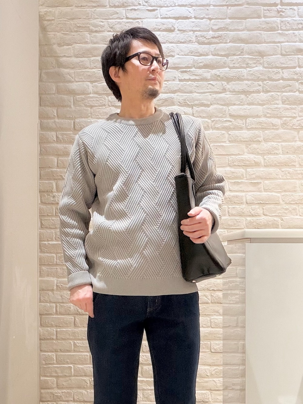 グレー系のニット/セーター、ブルー系のデニムパンツ、ブラック系のトートバッグを着用したメンズの冬コーディネートの2枚目の写真
