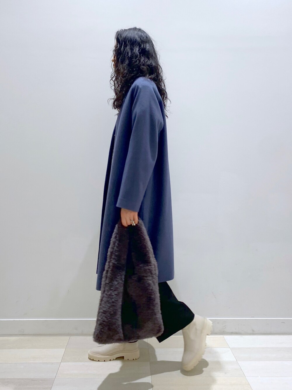 ブルー系のノーカラーコート、グレー系のニット/セーター、ブラック系のスラックスを着用したレディースの冬コーディネートの2枚目の写真