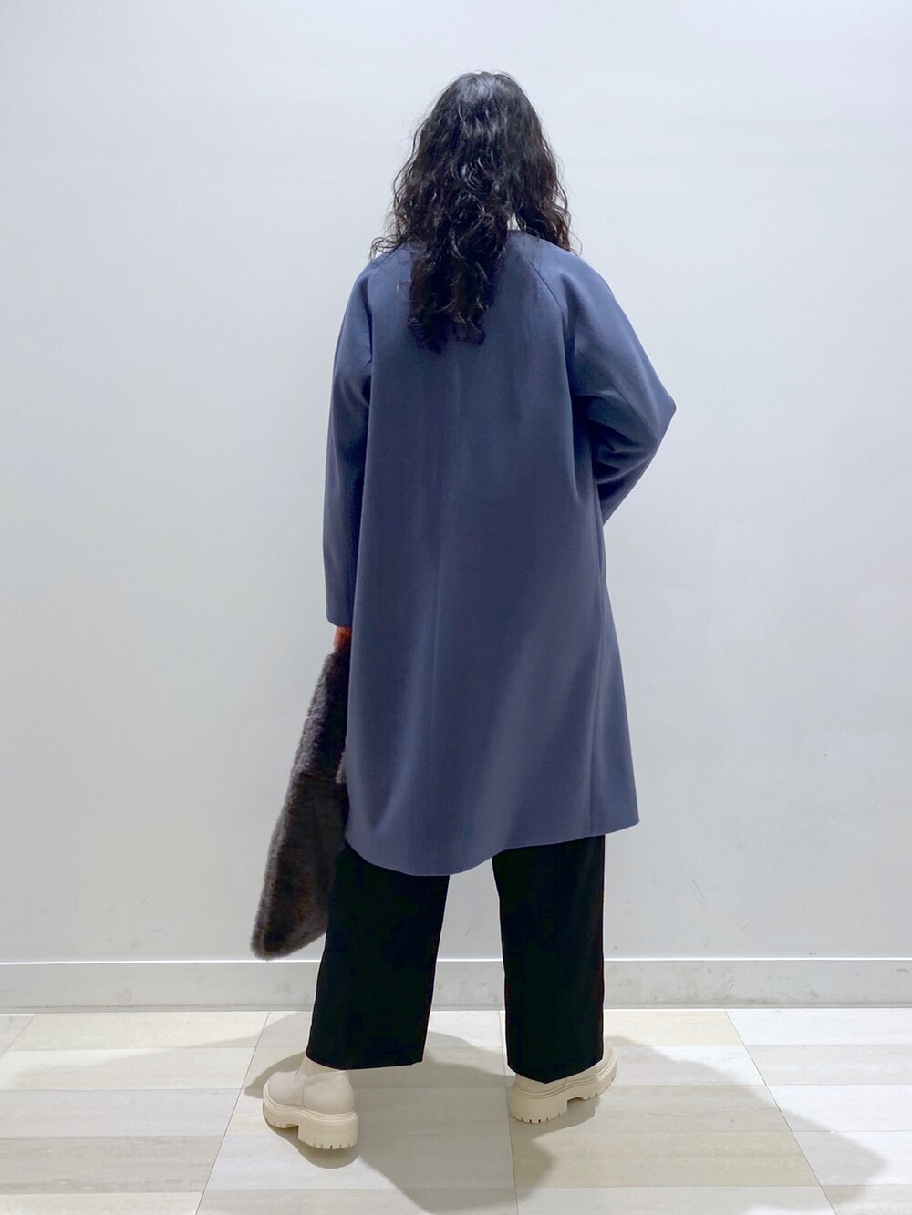 ブルー系のノーカラーコート、グレー系のニット/セーター、ブラック系のスラックスを着用したレディースの冬コーディネートの3枚目の写真