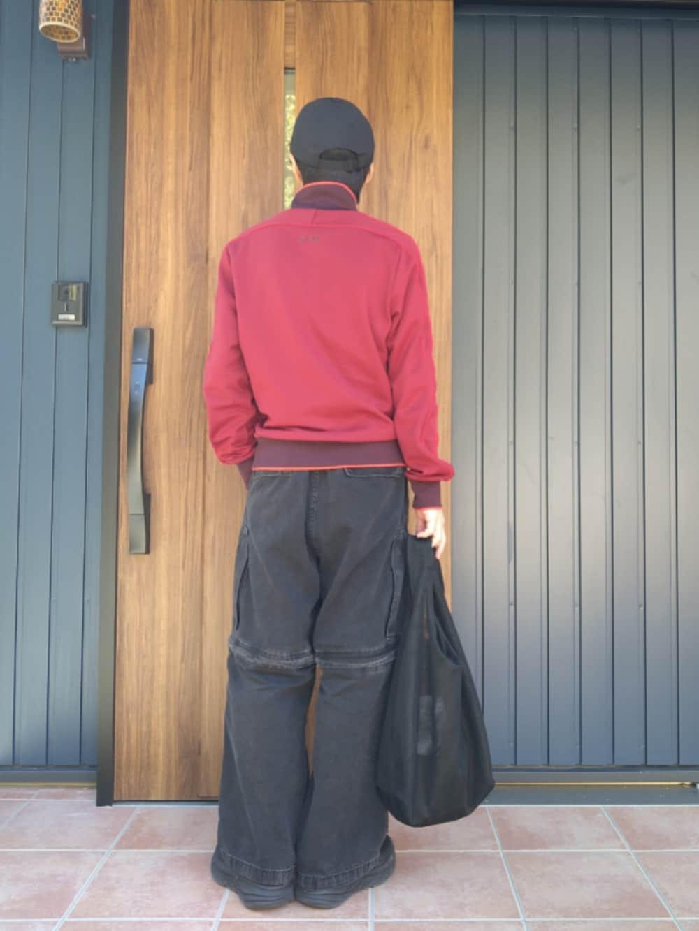 ブラック系のスニーカー、レッド系のジャージ、ブラック系のデニムパンツを着用したメンズの冬コーディネートの3枚目の写真