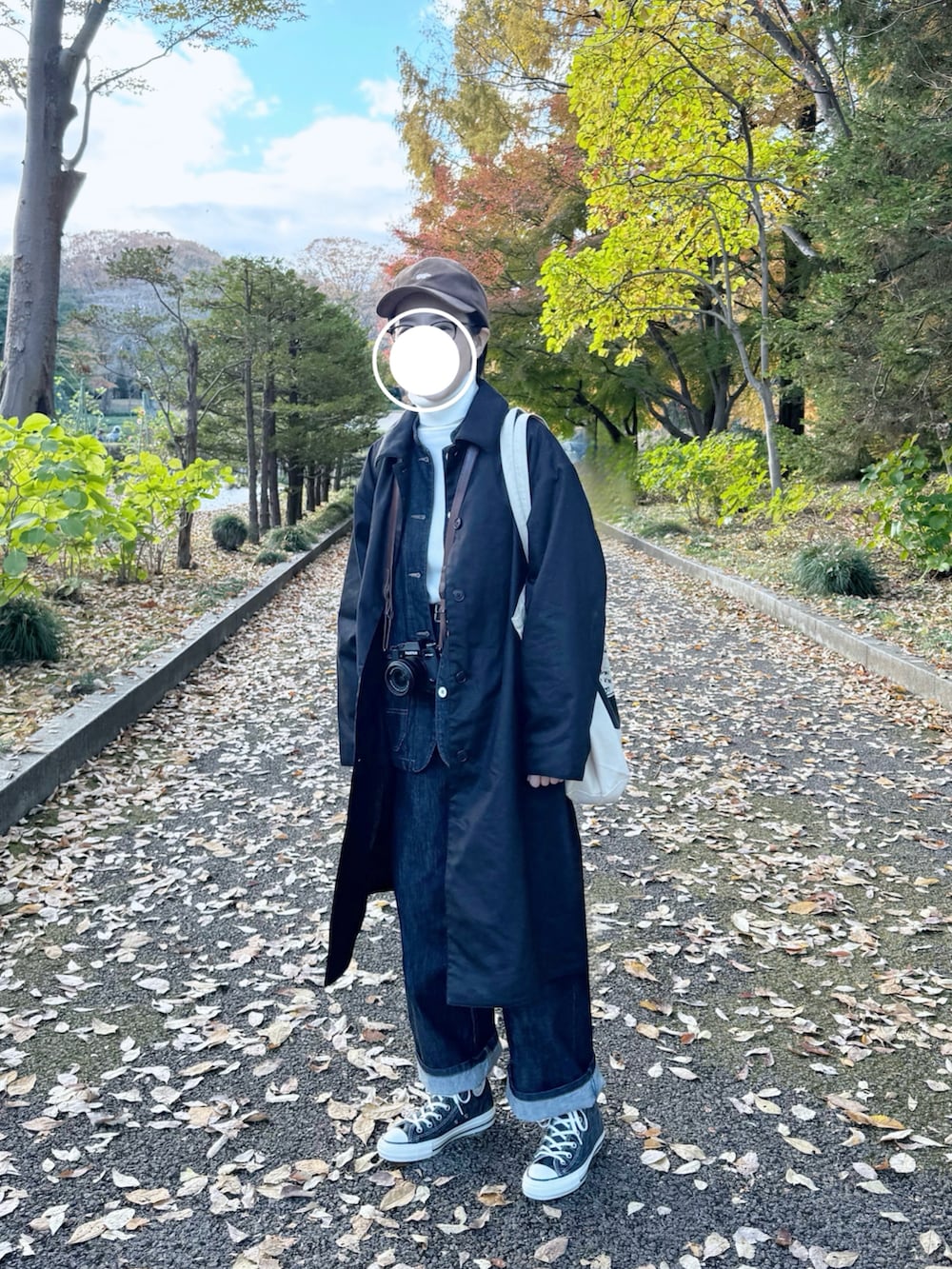 ブラック系のステンカラーコート、ブルー系のカバーオール、ブルー系のデニムパンツを着用したレディースの秋コーディネートの2枚目の写真