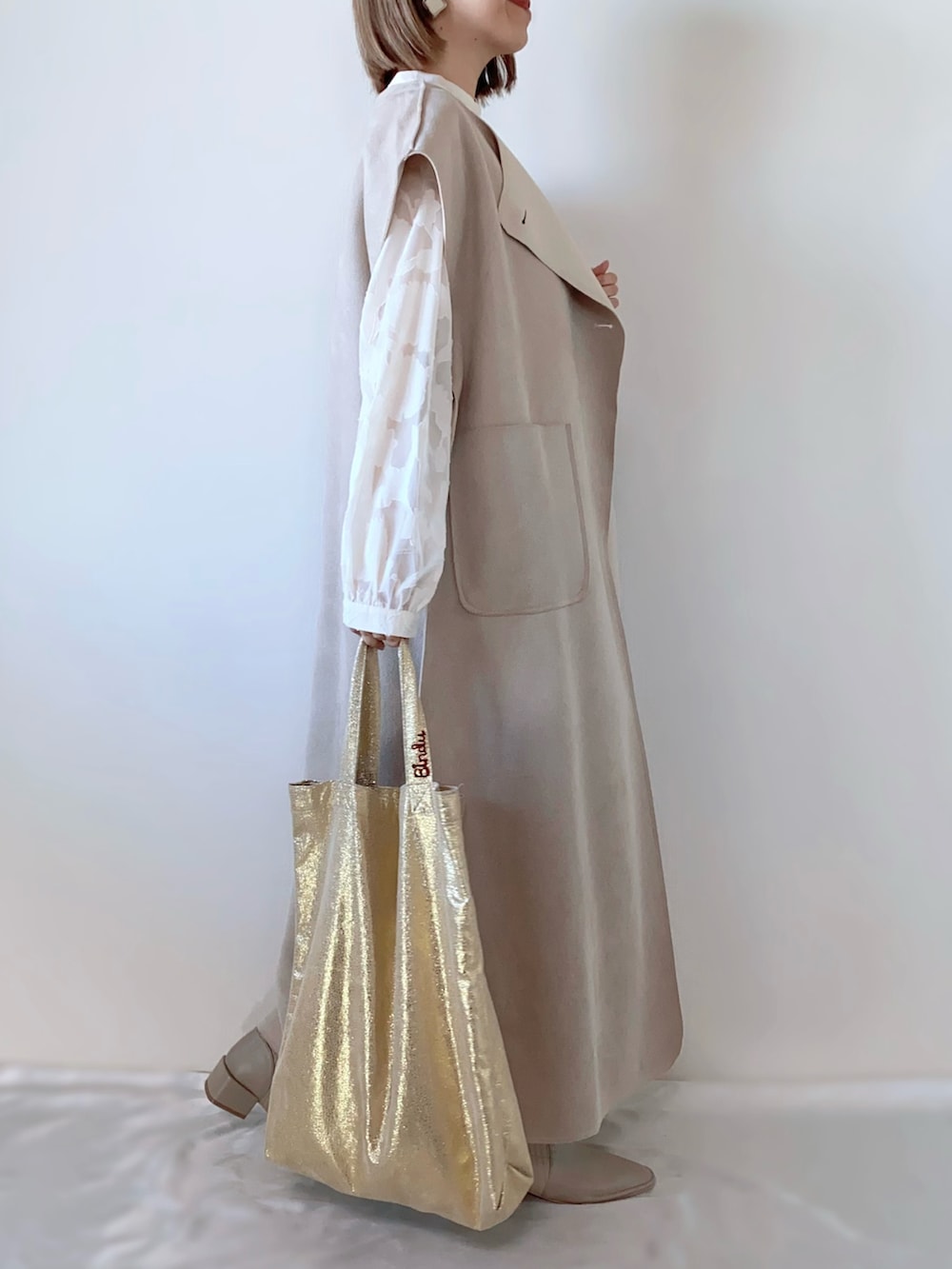 ホワイト系のドレス、ベージュ系のベスト、ゴールド系のトートバッグを着用したレディースの春コーディネートの2枚目の写真