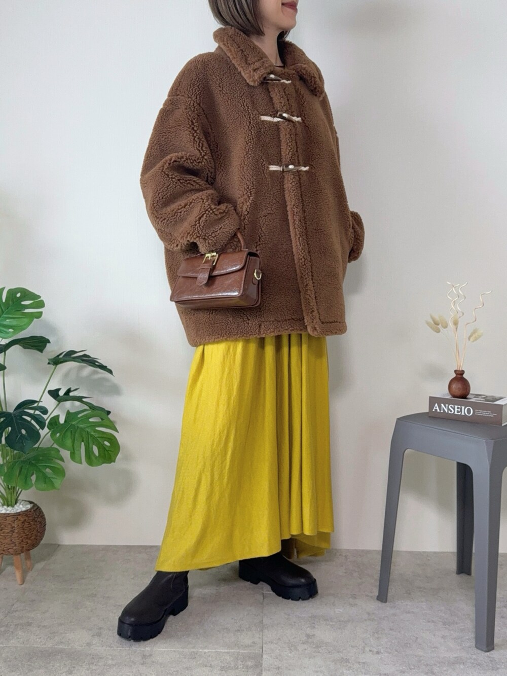 ブラウン系のムートンコート、ブラウン系のハンドバッグ、ブラウン系のブーツを着用したレディースの秋コーディネートの3枚目の写真