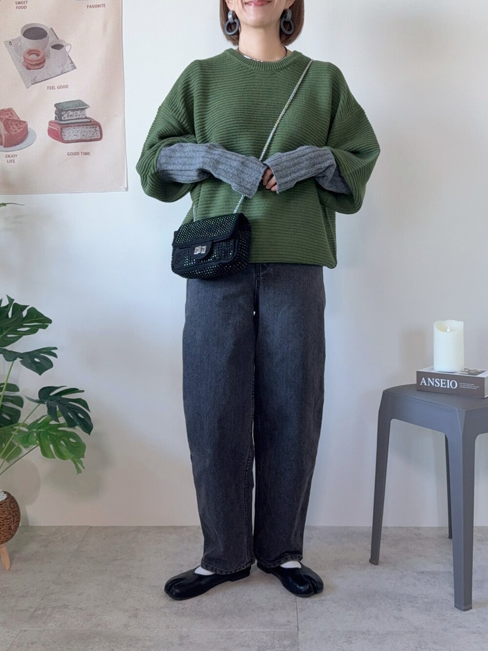 グリーン系のニット/セーター、ブラック系のデニムパンツ、ブラック系のクラッチバッグを着用したレディースの秋コーディネートの2枚目の写真