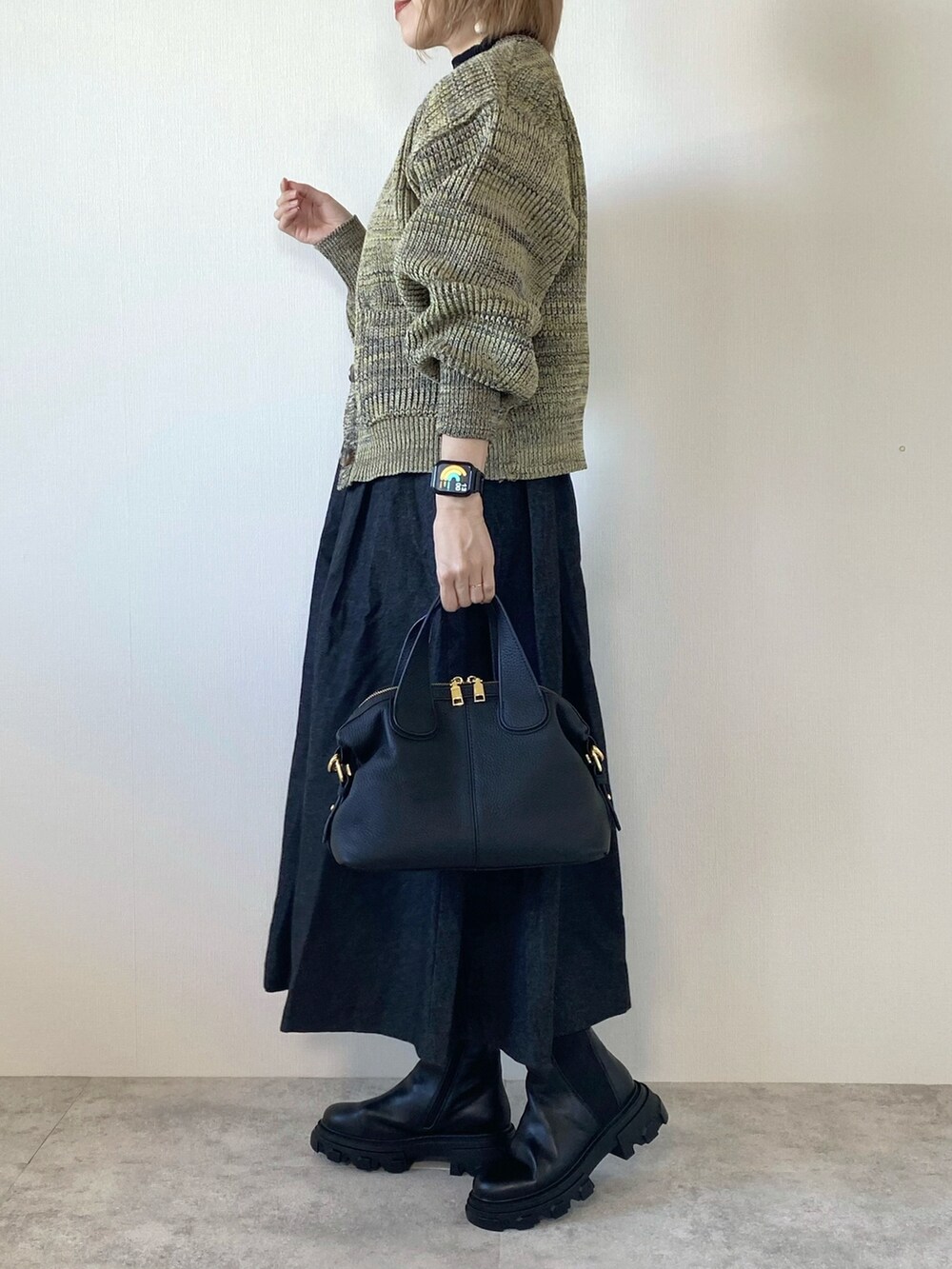 ブラック系のスカート、ブラック系のバッグ、ブラック系のブーツを着用したレディースの秋コーディネートの2枚目の写真