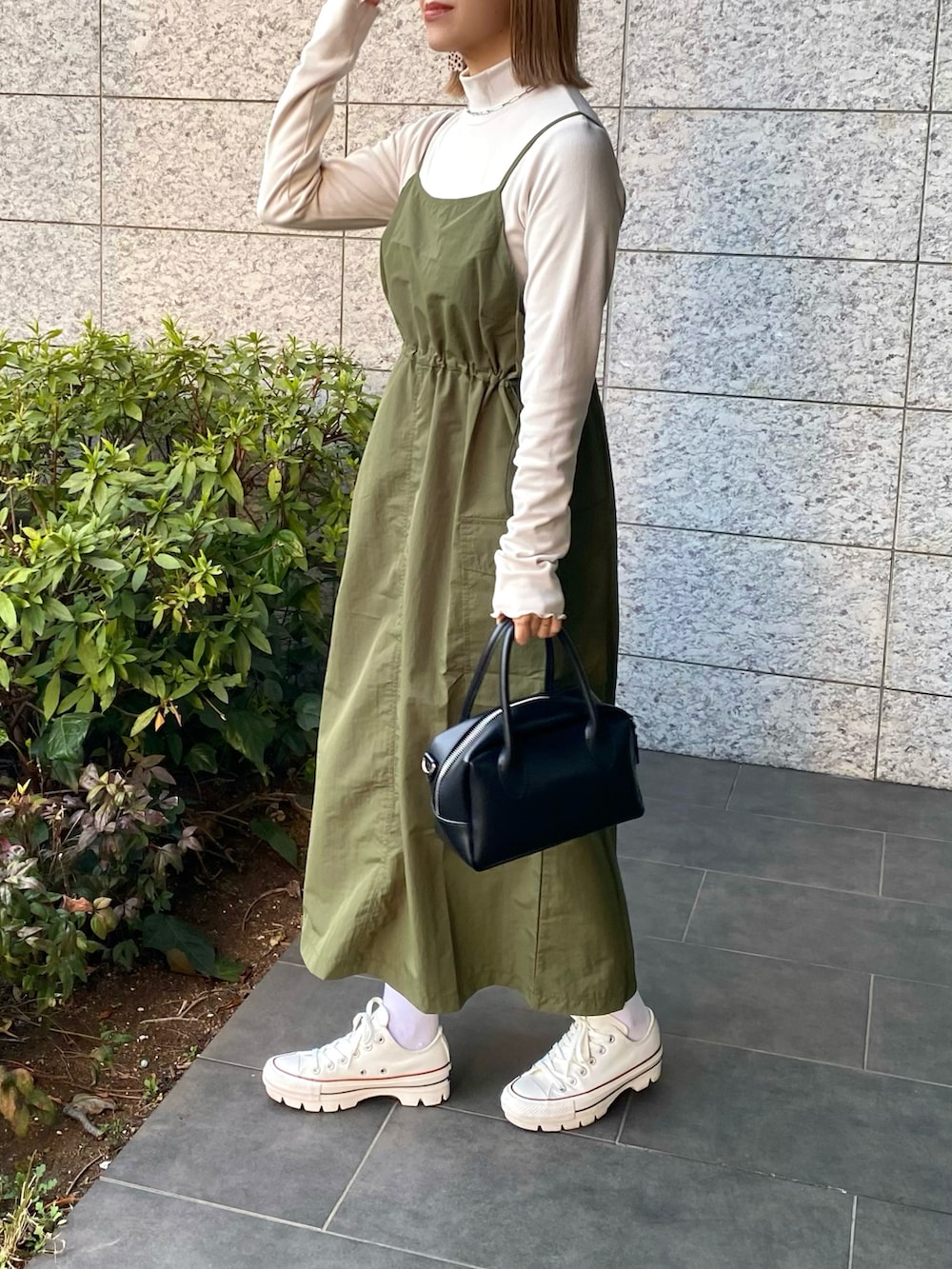 ブラック系のバッグ、グリーン系のワンピース、ホワイト系のスニーカーを着用したレディースの春コーディネートの2枚目の写真