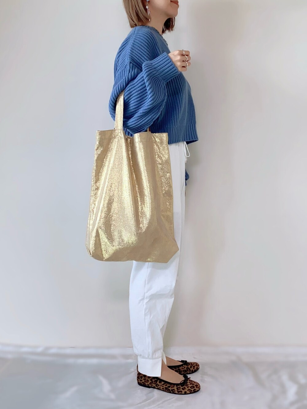 ゴールド系のトートバッグ、ホワイト系のその他パンツ、ブルー系のニット/セーターを着用したレディースの春コーディネートの2枚目の写真