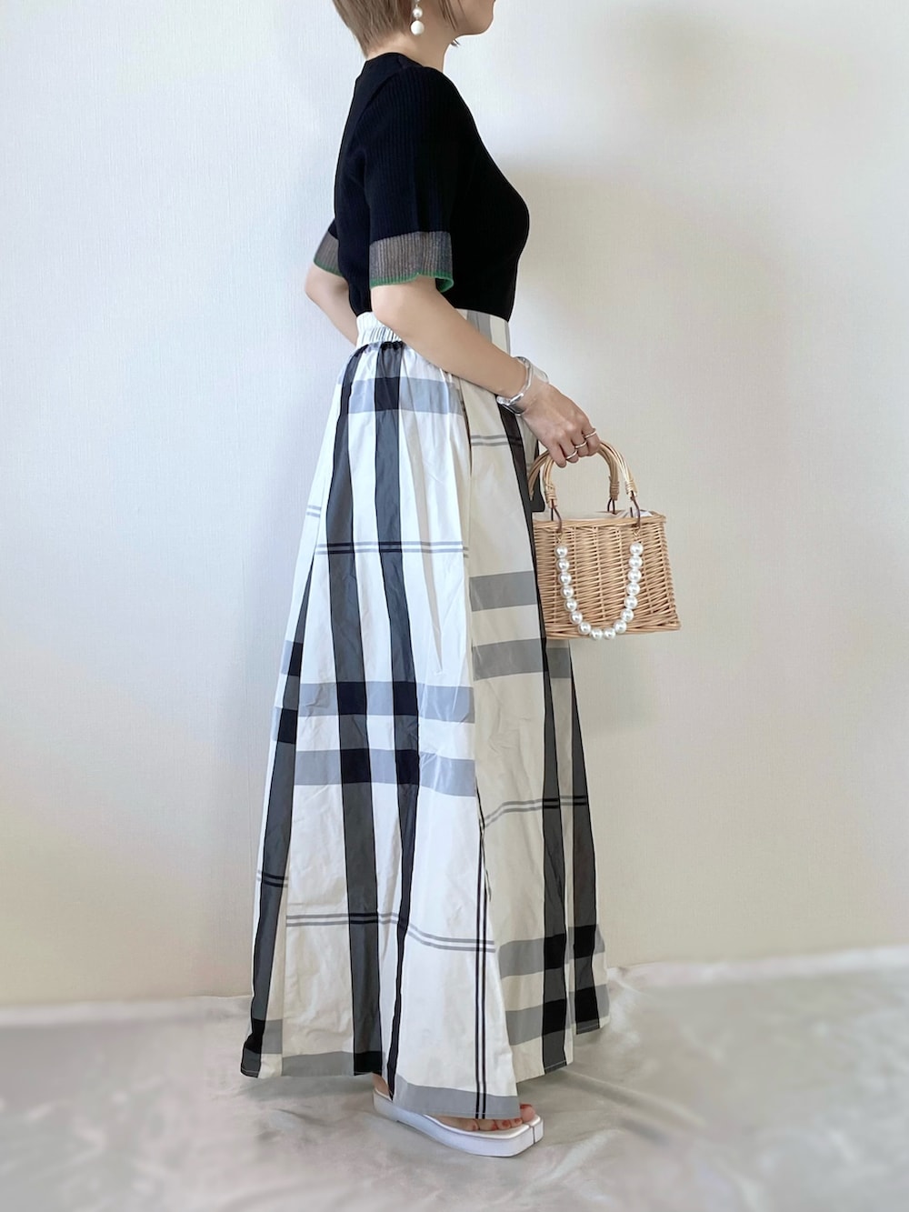 ブラック系のニット/セーター、ホワイト系のスカート、ベージュ系のかごバッグを着用したレディースの夏コーディネートの2枚目の写真