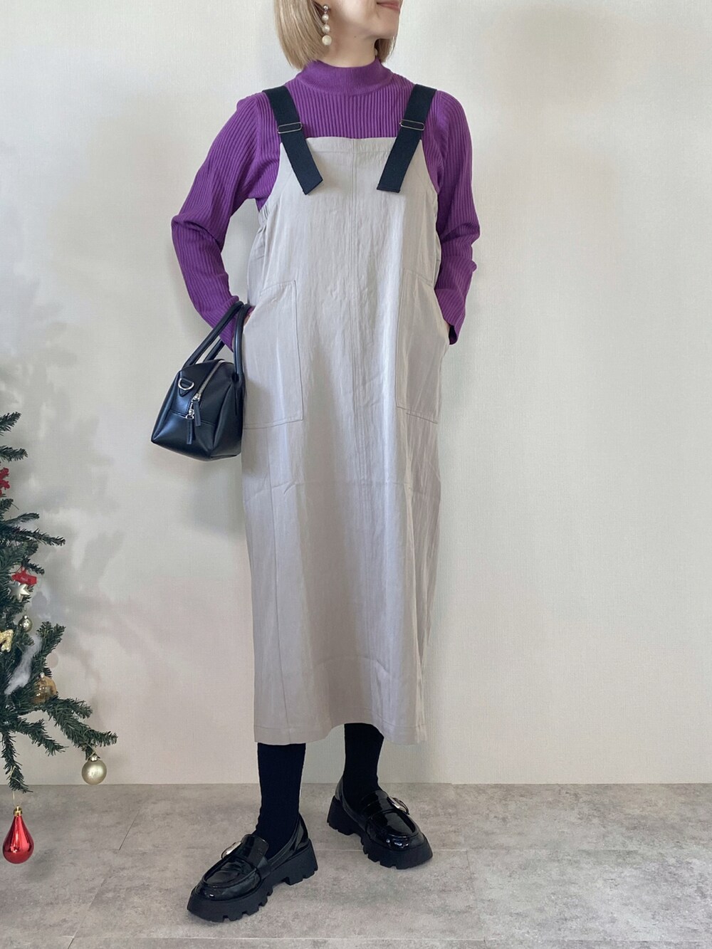 パープル系のニット/セーター、グレー系のジャンパースカート、ブラック系のバッグを着用したレディースの冬コーディネートの2枚目の写真