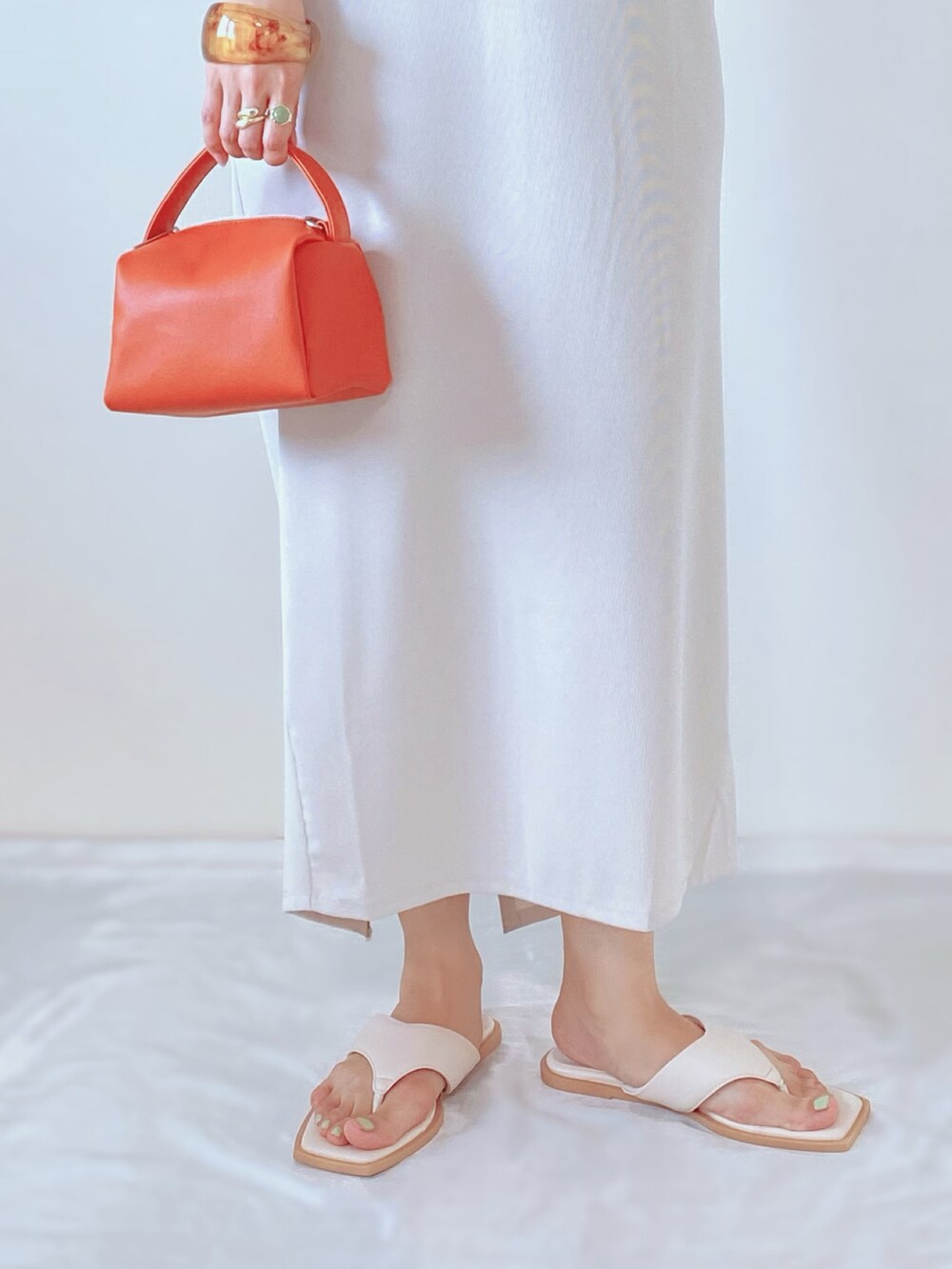 ホワイト系のサンダル、オレンジ系のバッグ、ベージュ系のワンピースを着用したレディースの夏コーディネートの3枚目の写真