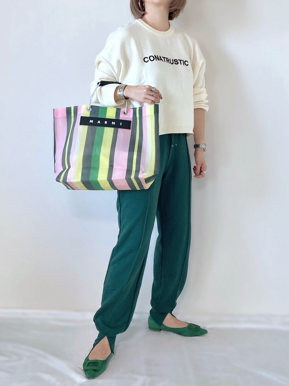 グリーン系のトートバッグ、グリーン系のパンプス、ホワイト系のニット/セーターを着用したレディースの秋コーディネートの2枚目の写真