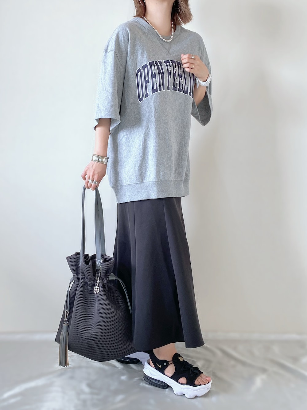 グレー系のバッグ、グレー系のTシャツ/カットソー、ブラック系のスカートを着用したレディースの夏コーディネートの2枚目の写真