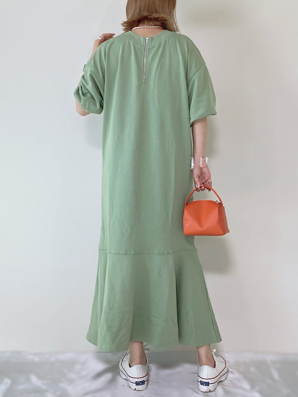 グリーン系のワンピース、オレンジ系のバッグ、ホワイト系のスニーカーを着用したレディースの春コーディネートの2枚目の写真