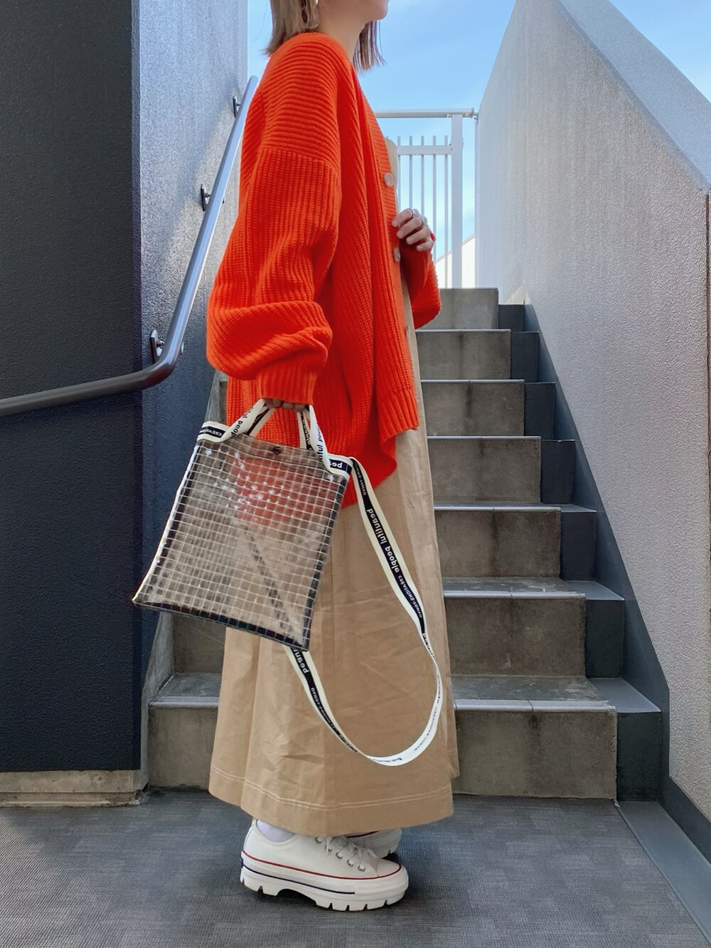 オレンジ系のカーディガン/ボレロ、ベージュ系のワンピース、ブラック系のショルダーバッグを着用したレディースの春コーディネートの2枚目の写真