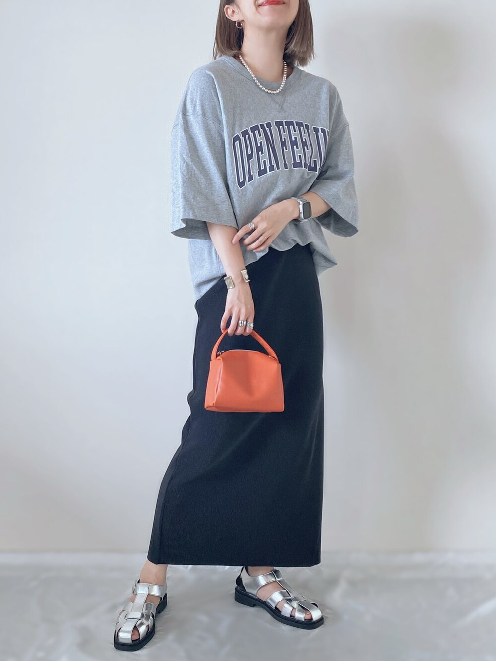 シルバー系のサンダル、オレンジ系のバッグ、ブラック系のスカートを着用したレディースの春コーディネートの2枚目の写真