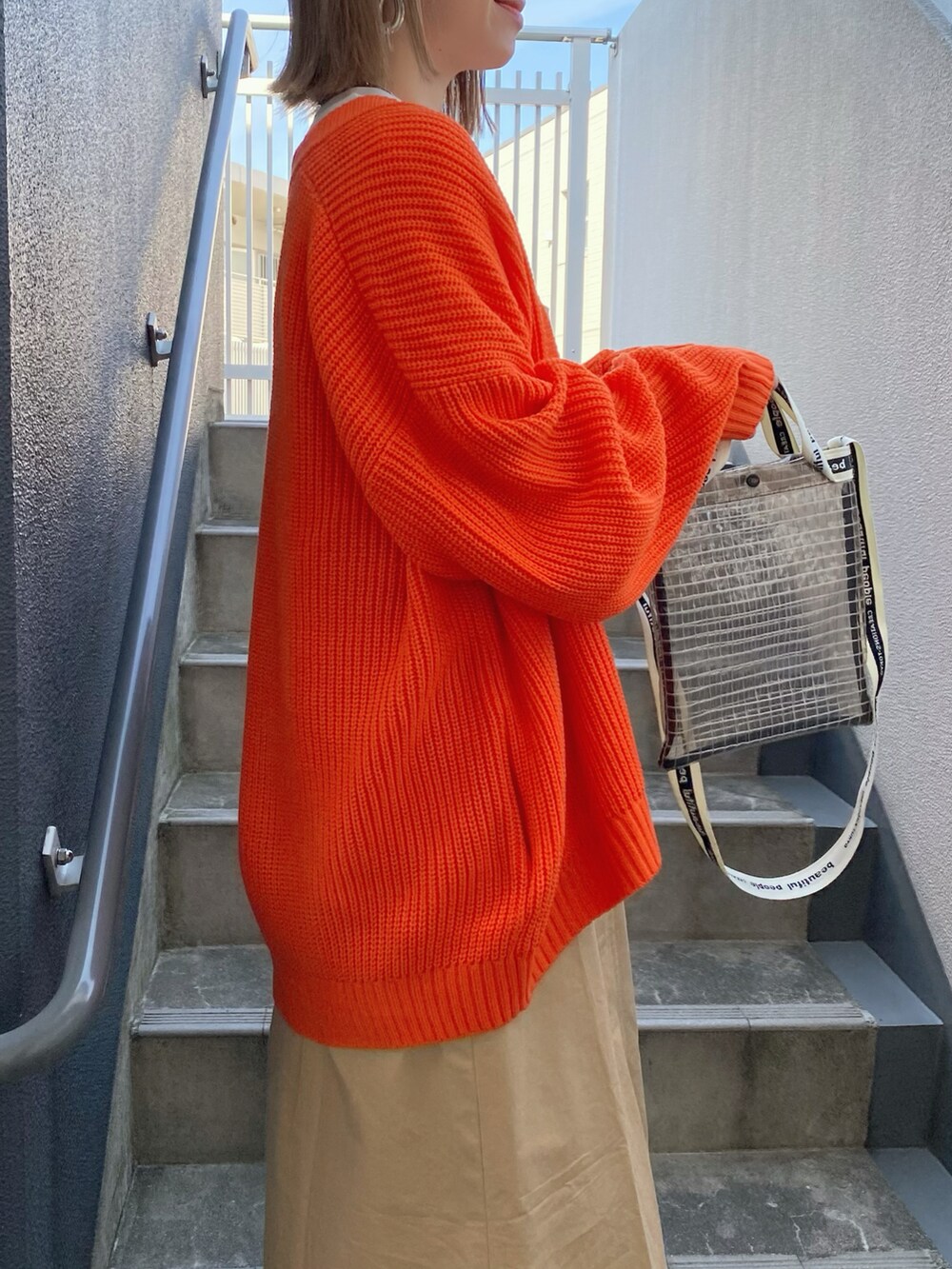 オレンジ系のカーディガン/ボレロ、ベージュ系のワンピース、ブラック系のショルダーバッグを着用したレディースの春コーディネートの5枚目の写真