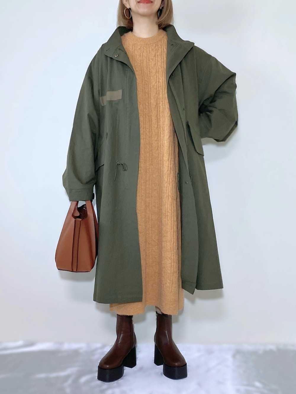 オレンジ系のワンピース、ブラウン系のバッグ、ブラウン系のブーツを着用したレディースの秋コーディネートの2枚目の写真