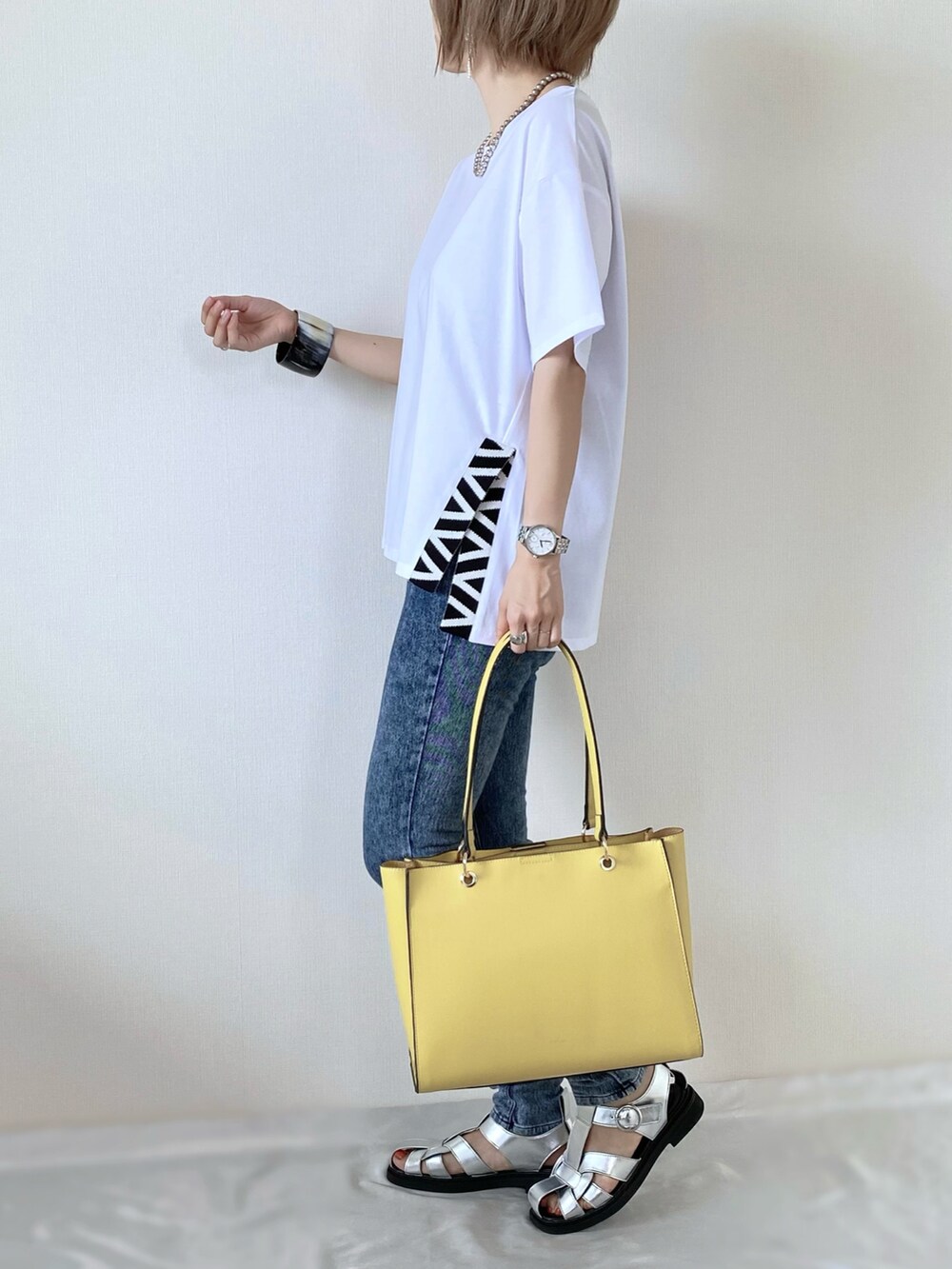 イエロー系のトートバッグ、ホワイト系のトップス、シルバー系のサンダルを着用したレディースの夏コーディネートの3枚目の写真
