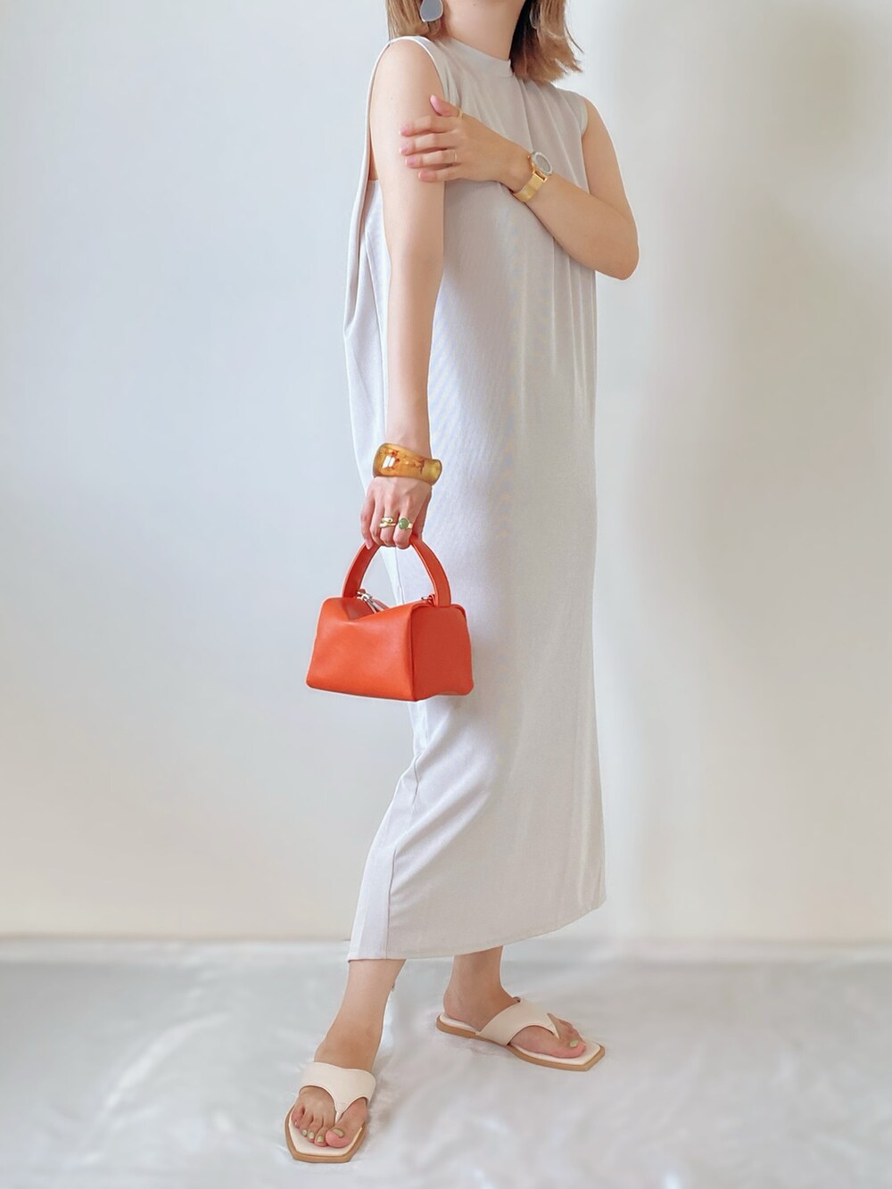 ホワイト系のサンダル、オレンジ系のバッグ、ベージュ系のワンピースを着用したレディースの夏コーディネートの2枚目の写真