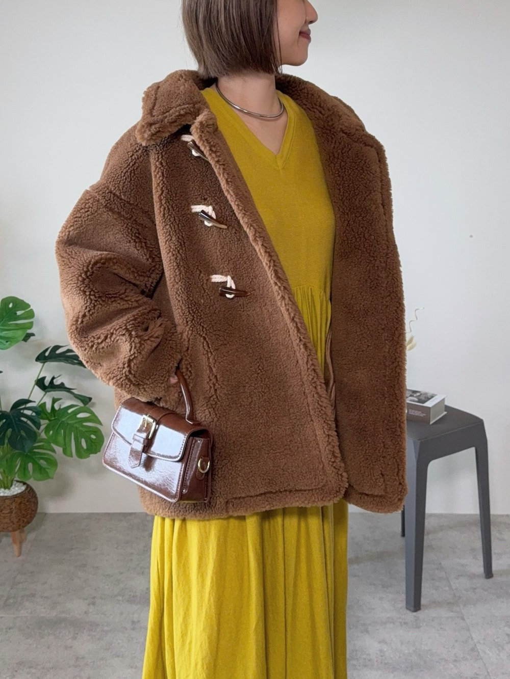 ブラウン系のムートンコート、ブラウン系のハンドバッグ、ブラウン系のブーツを着用したレディースの秋コーディネートの2枚目の写真