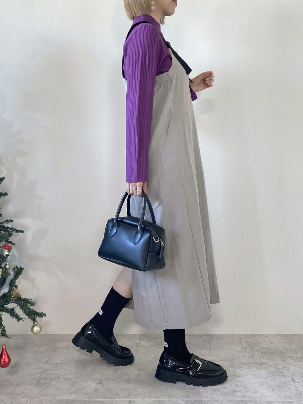 パープル系のニット/セーター、グレー系のジャンパースカート、ブラック系のバッグを着用したレディースの冬コーディネートの3枚目の写真