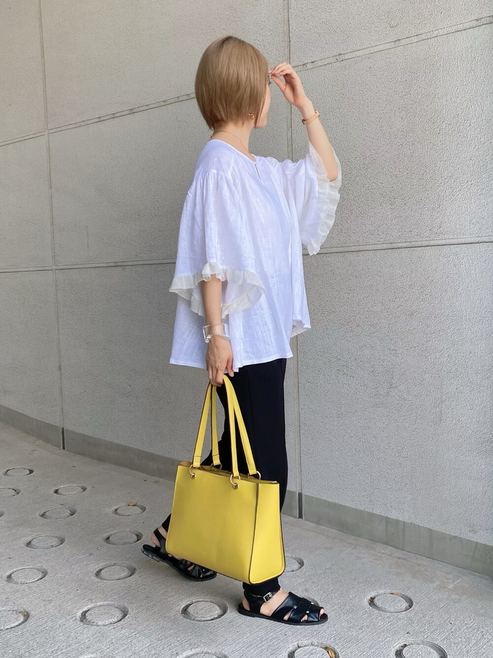 イエロー系のトートバッグ、ホワイト系のシャツ/ブラウス、ブラック系のパンツを着用したレディースの夏コーディネートの2枚目の写真