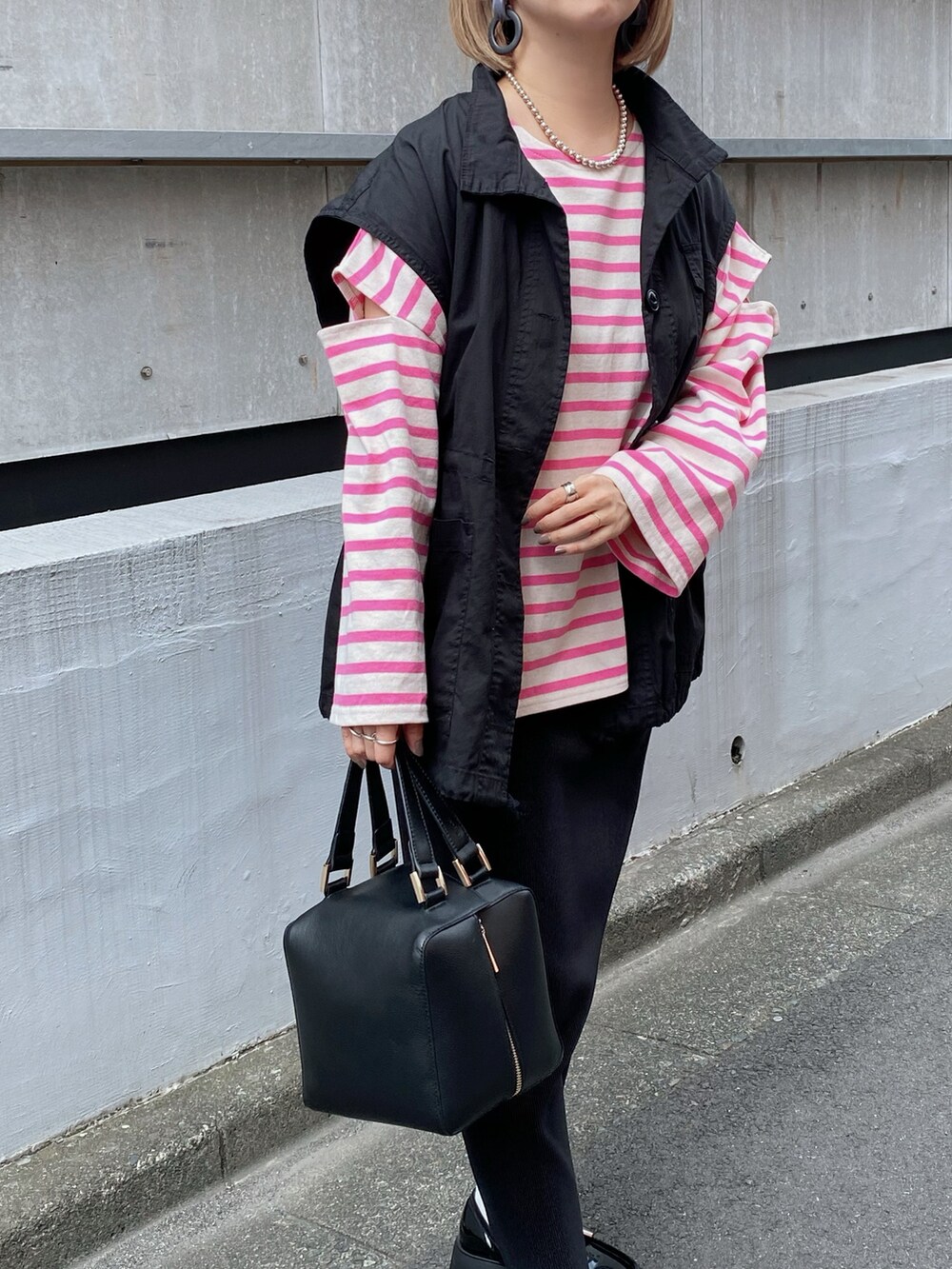 ブラック系のベスト、ピンク系のTシャツ/カットソー、ブラック系のハンドバッグを着用したレディースの秋コーディネートの2枚目の写真