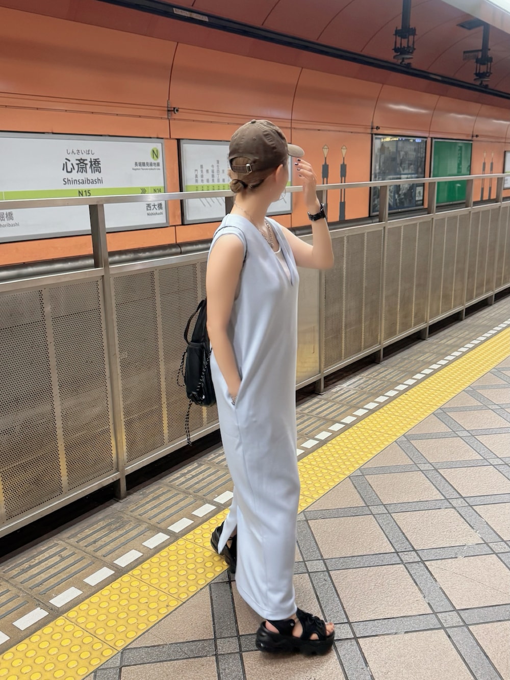 ブラック系のサンダル、ブルー系のジャンパースカート、ブラウン系のキャップを着用したレディースの秋コーディネートの4枚目の写真