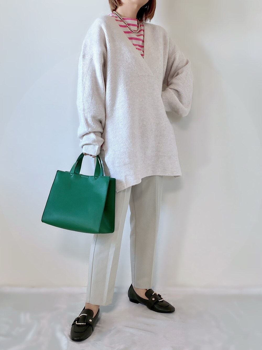 グリーン系のトートバッグ、ベージュ系のニット/セーター、ピンク系のTシャツ/カットソーを着用したレディースの秋コーディネートの2枚目の写真