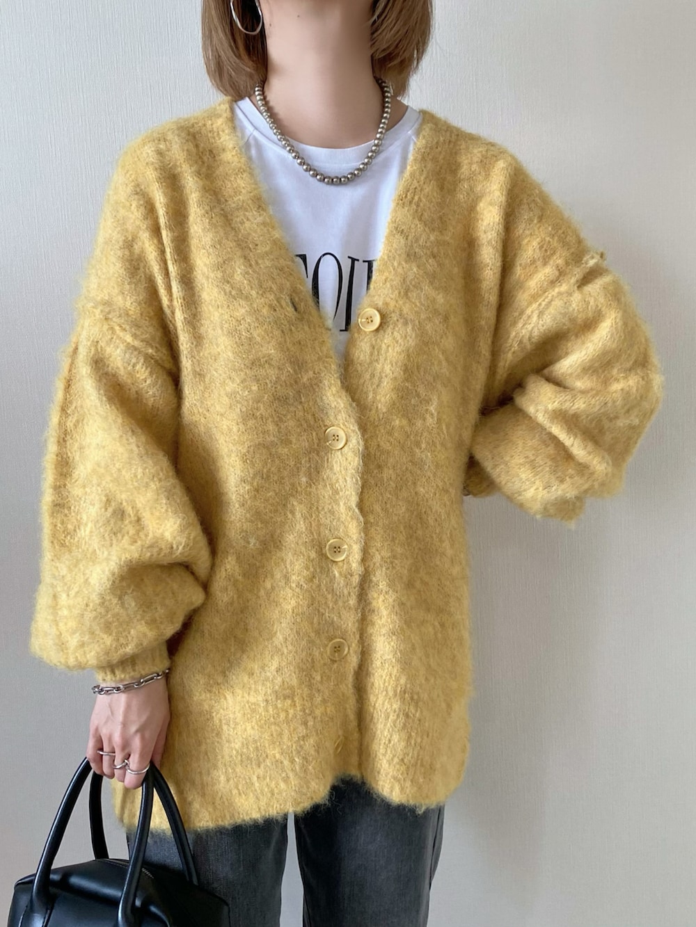 イエロー系のカーディガン/ボレロ、ブラック系のバッグ、グレー系のデニムパンツを着用したレディースの冬コーディネートの3枚目の写真