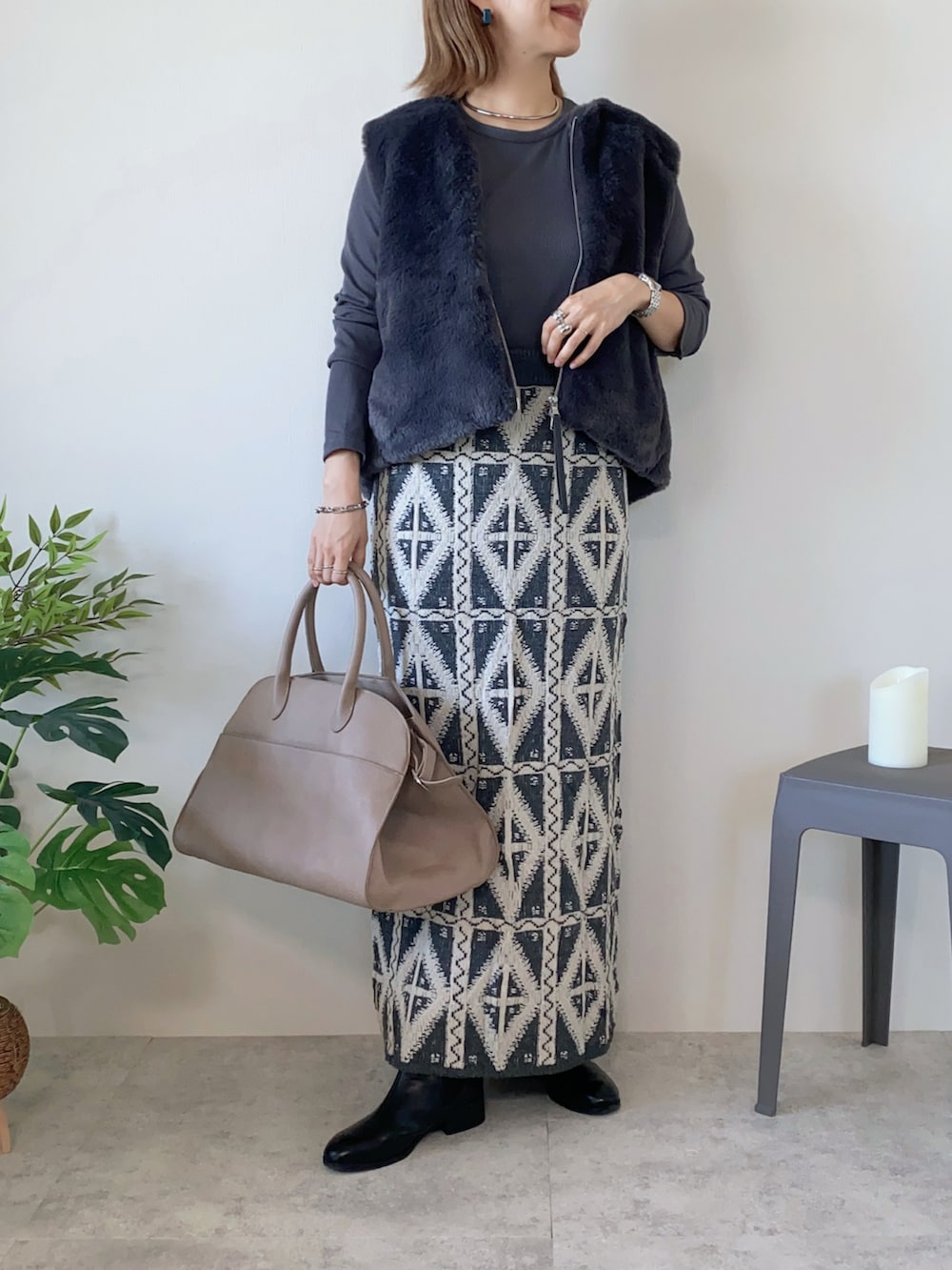 グレー系のベスト、ベージュ系のボストンバッグ、グレー系のスカートを着用したレディースの秋コーディネートの2枚目の写真